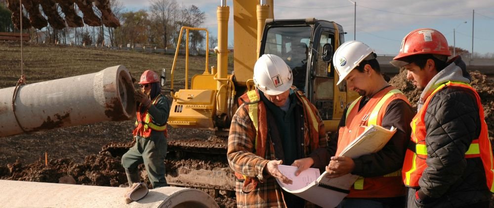 Project managers collaborating onsite while concrete pipe installation commences in the background.