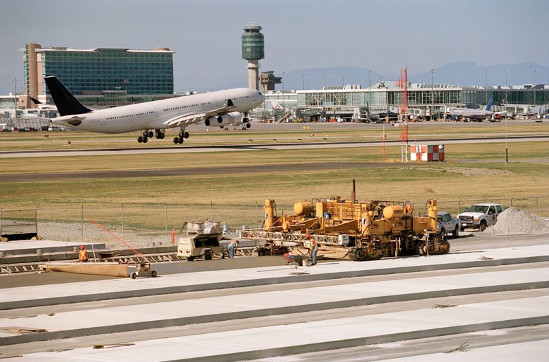 Concrete paving operation with active airport in background and an airplane taking off,