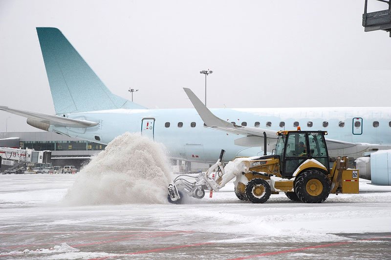 Rubber tire backhoe with sweaper attachment clears snow around an airplane.