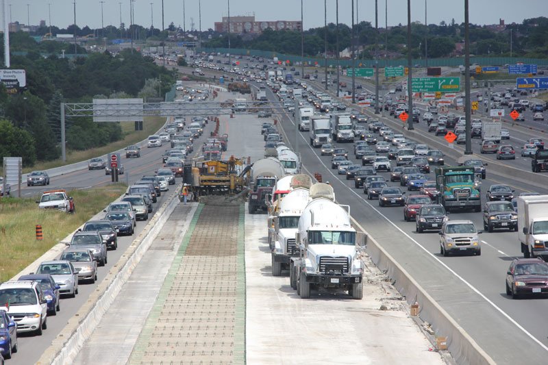 Concrete paving in work zone while heavy highway traffic surrounds the operation.